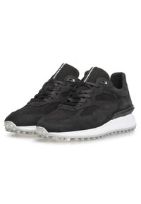Zapatillas deportivas negras que combinan materiales de ante y malla, con una punta redondeada, diseño con cordones y una entre suela blanca en contraste con un dibujo texturizado.