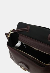 Sac à main en cuir bourgogne avec une finition texturée, compartiment principal zippé, doublure noire, quincaillerie dorée et accent circulaire à l'avant.