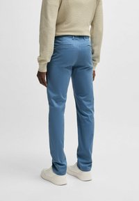 Blue cotton pants with a slim fit, smooth texture, and back pockets, paired with white sneakers and a light-colored sweater.