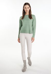 Mintgrüner Strickpullover mit geripptem Saum, kombiniert mit hellbeigen, figurbetonten Hosen und grauen Stiefeletten mit klobiger Sohle.