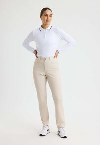 Vit långärmad polo med svart krage, kombinerad med ljusbeiga tapered byxor med ett subtilt diamantmönster och vita sneakers.