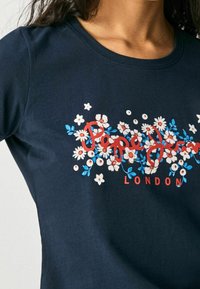 Námořnické bavlněné tričko s květinovým potiskem v bílé, modré a červené barvě, s textem "Pepe Jeans LONDON" integrovaným do designu.