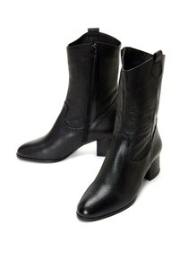 Paire de bottes en cuir noir montant jusqu'au milieu du mollet avec talons blocs et fermeture éclair latérale, surface texturée, bouts légèrement pointus sur fond blanc.
