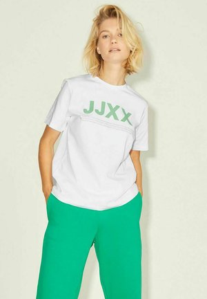 Camiseta blanca de manga corta con el texto verde "JJXX" en la parte frontal. Combinada con pantalones verdes de corte holgado, que presentan una textura suave y un diseño casual.