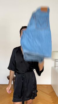 Denimski kombinezon v svetlo modri barvi, ki ima nastavljive naramnice, sprednji žep in surov rob. Tkanina ima gladko teksturo.