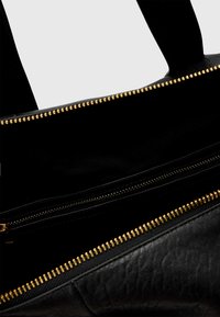 Black handbag with gold zippers, featuring a spacious interior and multiple compartments. Smooth texture and sturdy handles.