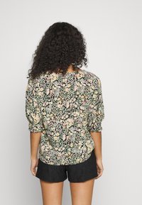 Blusa floral com mangas curtas e bufantes em preto, apresentando um padrão floral multicolorido. Usada com calções pretos.