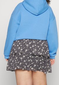 Sininen huppari, joka on yhdistetty kerrokselliseen mustaan kukkakuosisesti hameeseen, jossa on valkoisia ja keltaisia kukkia. Pehmeä kangas, rento muotoilu.