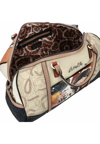 Sac de sport avec une surface beige clair texturée, des accents marron et un design graphique coloré. L'intérieur présente une doublure à motifs et une poche zippée.