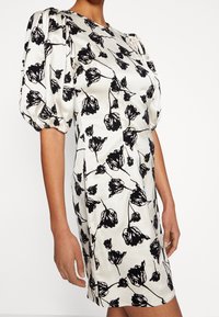 Robe ajustée à manches courtes en tissu lisse crème avec imprimé floral noir et manches bouffantes. Elle présente un col rond et un ourlet droit.