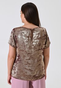 Top a maniche corte in tessuto texturizzato oro e bordeaux, con chiusura a fessura sul retro e vestibilità rilassata. Sheen a motivo in tutto il capo.