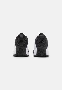 Chaussures de sport noir et blanc avec une tige en mesh, un col rembourré, une languette de traction et une semelle en caoutchouc texturée avec un motif en zigzag.