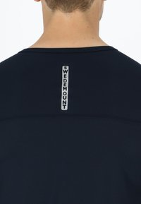 Achteraanzicht van een persoon die een donkerblauw shirt draagt met een verticale "Swedemount"-logo in lichtgrijs gedrukt op de bovenrug.