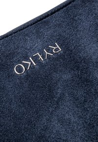 Tessuto strutturato blu navy con un logo argento "PRYLIKO" in rilievo sulla superficie, incorniciato da un bordo in pelle liscia.