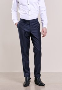 Pantaloni eleganti a righe blu navy, con una texture liscia e taglio dritto, indossati con una camicia bianca e scarpe in pelle nere.