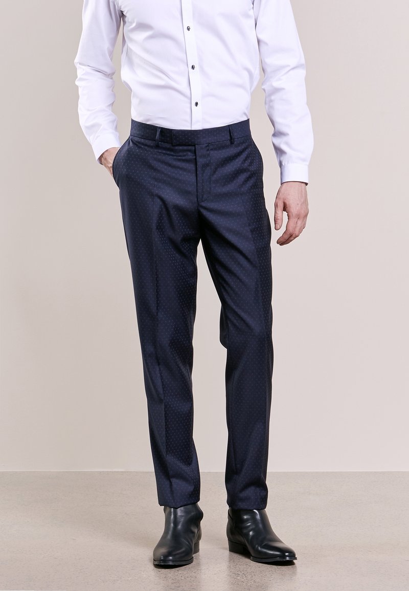 Pantaloni eleganti a righe blu navy, con una texture liscia e taglio dritto, indossati con una camicia bianca e scarpe in pelle nere.