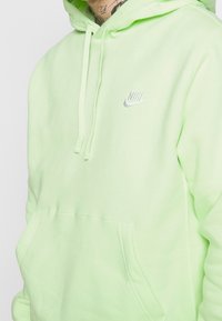 Ljusgrön hoodie med en känguruficka, dragsko och en liten silvrig Nike-logga på bröstet. Tillverkad i mjukt, texturerat material.