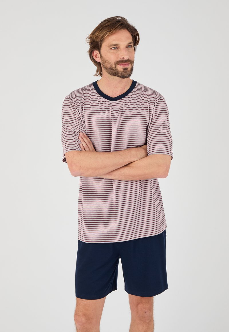 Gestreept shirt met korte mouwen in rood en wit met marineblauwe accenten, gecombineerd met marineblauwe shorts. Het shirt heeft een v-hals en een relaxte pasvorm.
