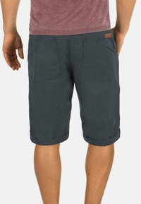 Shorts en coton gris foncé avec des ourlets roulés, comprenant deux poches arrière et une petite étiquette en cuir brun près de la taille.