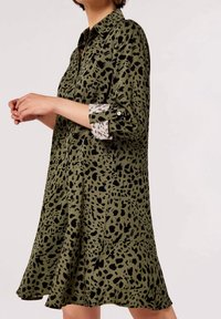 Grøn kjole med sort abstrakt print. Har krave, knappede ærmer med kontrasterende leopardprint-manchetter og en skørtekant, der flæser.