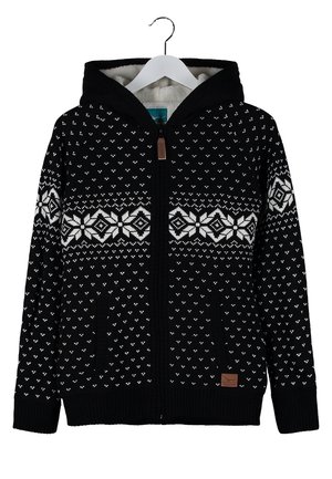Persoon die loopt, draagt een zwart-wit patroon zip-up hoodie, wit hemdje, blauwe spijkerbroek en zwarte sneakers met kleurrijke details.