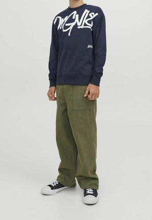 Sweatshirt bleu marine avec texte graphique blanc, associé à un pantalon cargo large vert. Des baskets noires et blanches complètent la tenue.