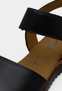 Μαύρο δερμάτινο σανδάλι με φαρδιά λουράκια στην επάνω πλευρά, ανοιχτό σχέδιο και υφασμένη ταμπά εσωτερική σόλα. Διαθέτει ανάγλυφα στοιχεία μεγέθους και πλάτους.