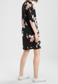 Svart klänning med korta ärmar som har ett blommönster i rosa och vitt. Mjuk tyg och lös passform, tillsammans med vita sneakers.