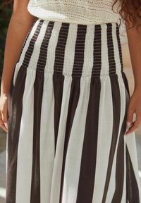 Jupe rayée noir et blanc avec une taille smockée, présentant un design fluide et un tissu léger et texturé. Taille élastique pour le confort.