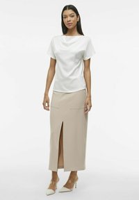 Hvit bluse med korte ermer, parret med en beige knelang skjørt med slisse foran og to frontlommer. Gjennomsiktige hæler.