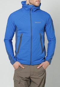 Veste softshell bleue à coupe ajustée, avec des accents gris, des poches zippées et une capuche pour plus de fonctionnalité. Texture lisse.