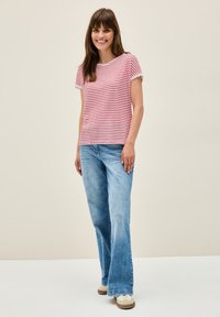 Camiseta de rayas rojas y blancas de manga corta, combinada con jeans acampanados de color azul claro y zapatillas color beige con cordones blancos, sobre un fondo neutro.