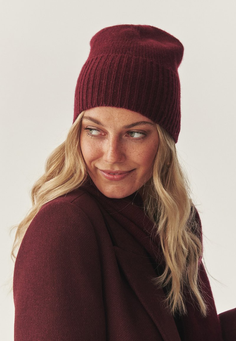Burgundowa wełniana czapka beanie o ribbowanej fakturze. Ma luźny design, miękki materiał i lekko przerośnięty kształt.