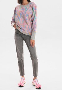 Sweat-shirt à motifs colorés dans des tons pastel avec des poignets gris, associé à un jean gris et des baskets roses, présentant une coupe décontractée et un col rond.