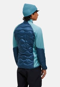 Blå og teal hybridjakke med en quilted bagside, glat polyesterforran og ribstrikket hue. Teksturerede finish giver designet et ekstra løft.