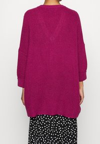 Pull en maille magenta avec une coupe décontractée, épaules tombantes et poignets côtelés. Tissu texturé et design avec un ourlet arrière plus long.