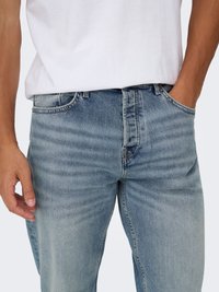 Vaqueros de denim azul claro con un acabado desgastado, corte recto y diseño de cinco bolsillos, combinados con una camiseta blanca básica.