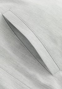 Material gri deschis cu o textură netedă, având o buzunare oblic. Coaserea este subtilă și completează designul general.