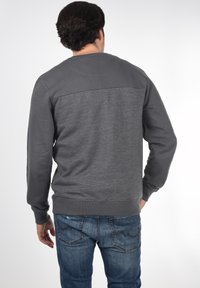 Grå sweatshirt med et strukturert, lysere grå panel på øvre rygg, ripete mansjetter og søm. Bært med blå denimjeans.