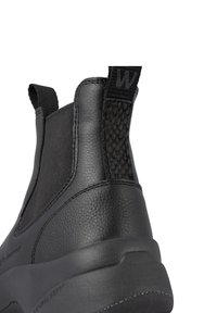 Botín negro con parte superior de cuero texturizado, paneles laterales elásticos y un detalle tejido en el tacón para mayor agarre.