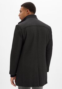 Schwarzer Mantel mit strukturiertem Stoff, strukturiertem Kragen und langen Ärmeln. Verfügt über einen klaren, geraden Schnitt mit minimalen Steppdetails.