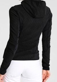 Zwarte hoodie met een gestructureerd, diamantpatroon. Strakke pasvorm met lange mouwen, voorzien van een capuchon en een gladde stoffen afwerking.