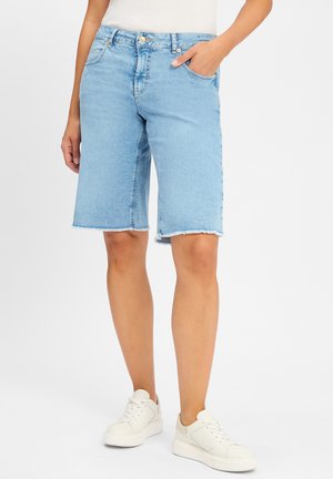 Bermuda shorts in denim azzurro chiaro con orlo sfrangiato, tasche frontali e chiusura con bottone, abbinati a sneaker bianche.