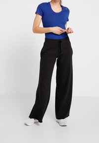 Top azul de manga corta combinado con pantalones de chándal negros de pierna ancha. Presenta una cintura con cordón, tejido suave y zapatillas blancas.