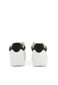 Witte sneakers met zwarte suède accenten, voorzien van een verhoogd, gegolfd ontwerp op de hiel, een gladde textuur en een dikke, witte zool.