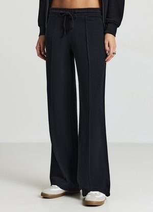 Pantalons de survêtement larges noirs avec une taille élastique et un cordon de serrage. Présente des détails de couture subtils et une texture lisse et douce.