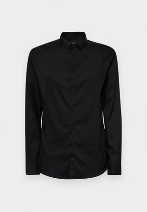 Musta pitkähihaisilla napitettava paita, joka on valmistettu sileästä kankaasta. Paidassa on klassinen kaulus, etunapit ja huomaamaton logo vasemman rintapihan yläpuolella.