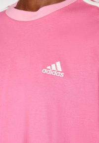 Rosa kortärmad t-shirt i bomull, med en kontrasterande ljusrosa halsringning och en vit Adidas-logotyp på bröstet.