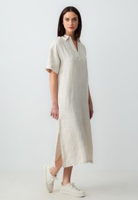 Linnen jurk in lichtbeige met een kraaghalslijn, korte mouwen, zijsplitten en een losse pasvorm, gecombineerd met witte sneakers.
