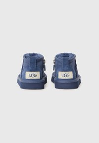 Bottines bleues en cuir suédé avec un intérieur moelleux, des zips de chaque côté et une étiquette crème affichant le logo UGG à l'arrière.